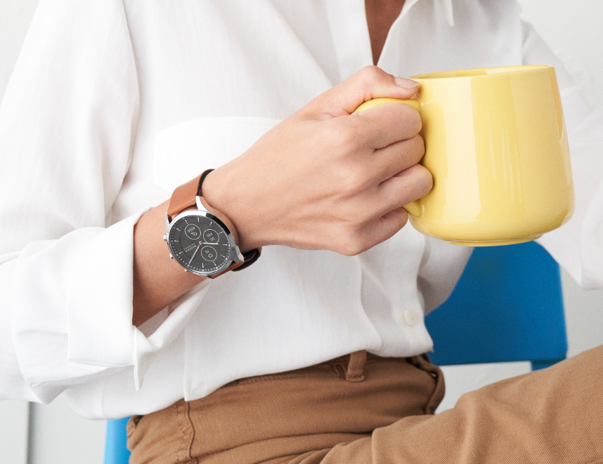 Minimalist-style man wearing Skagen watch featuring brown-leather strap. Minimalist-style woman wearing Skagen watch featuring brown-leather strap.