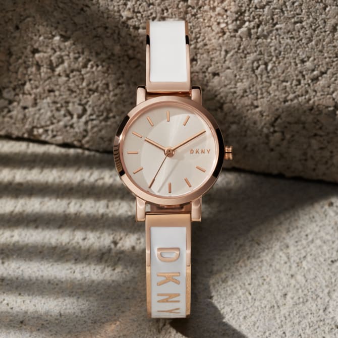 Von Schmuck inspirierte DKNY Uhren. Eine Uhr mit einem weißen, emaillierten Armreif und eine Uhr mit einem überkreuzten Band.