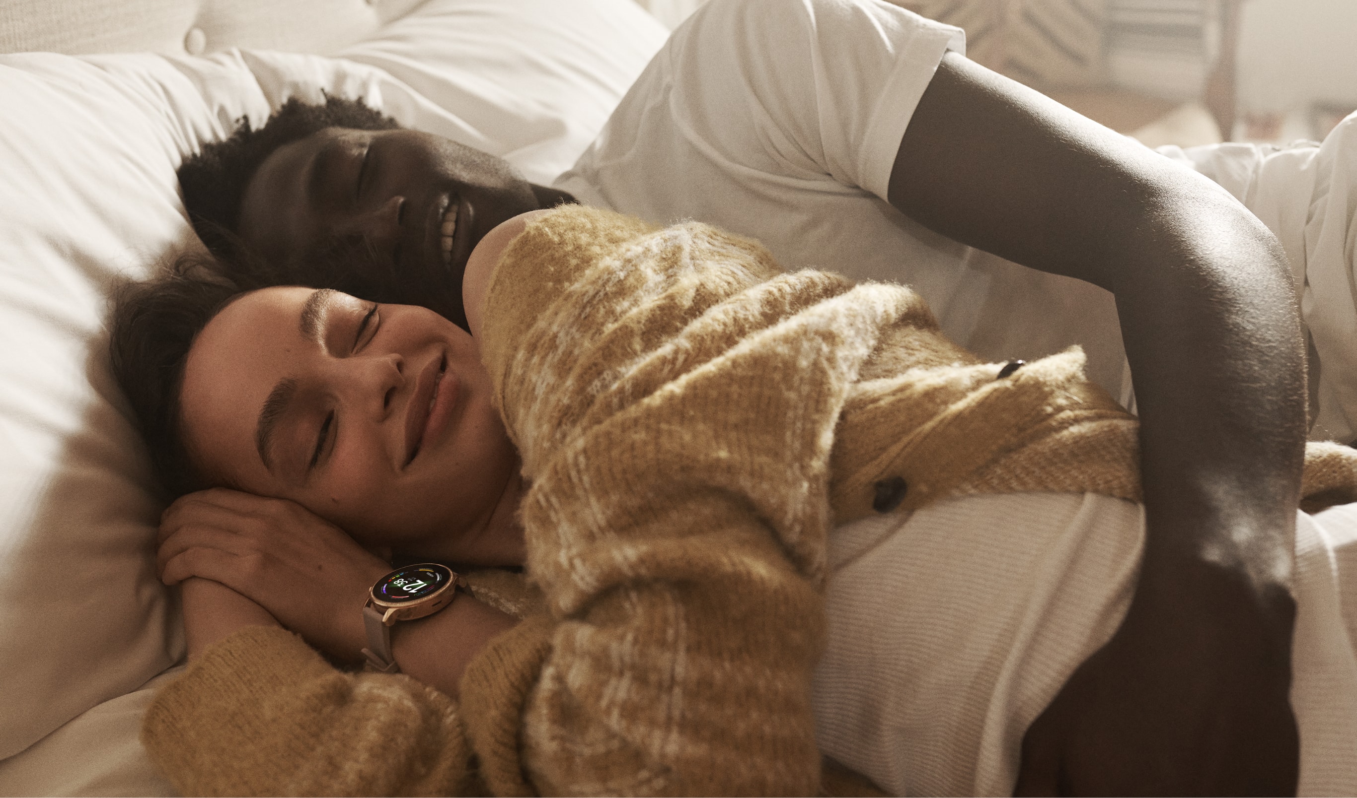 A man and a woman taking a nap with a Gen 6 smartwatch showing colourful charging rings. 