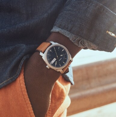 Tight shot of man in denim shirt and orange pants with hand in pocket wearing a Fossil men’s watch