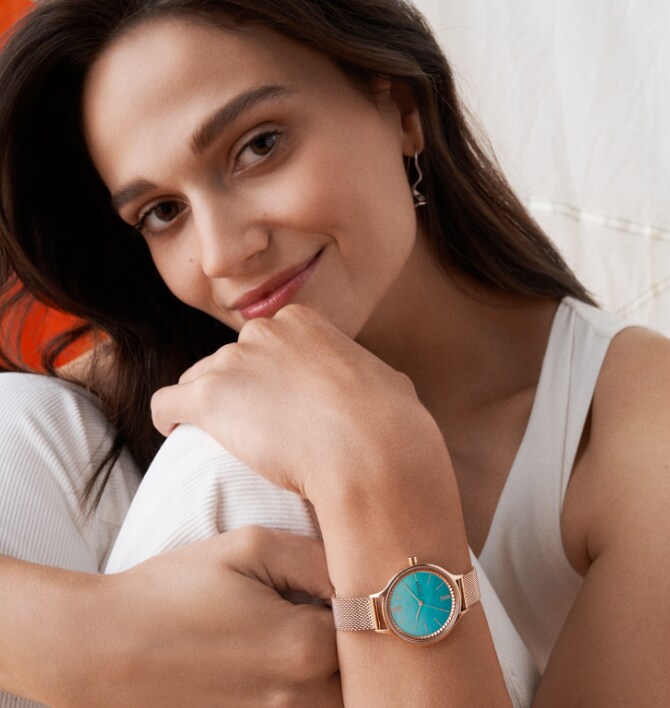 Minimalist-style woman wearing rose gold-tone and teal Skagen watch.